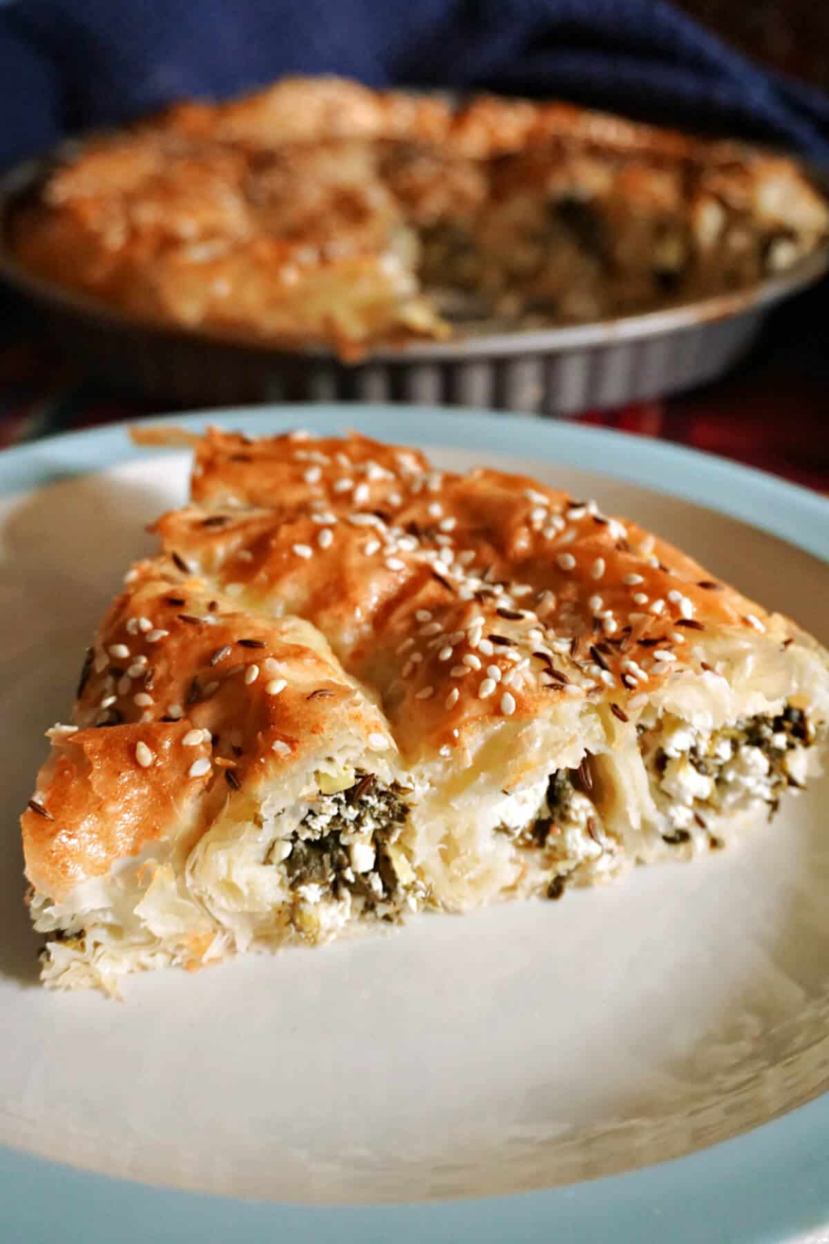 A slice of cheese and spinach pastry on a white plate.