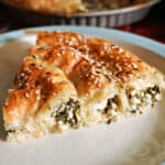 A slice of cheese and spinach pastry on a white plate.