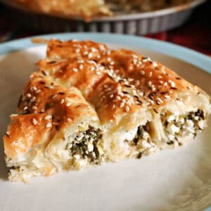 A slice of cheese and spinach pastry on a white plate.