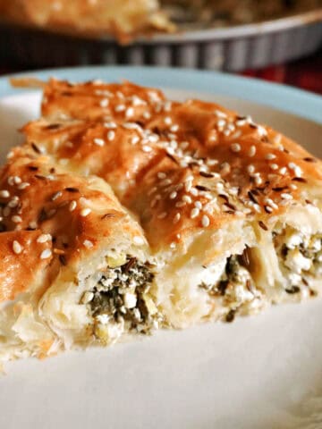 A slice of cheese and spinach pastry on a white plate.