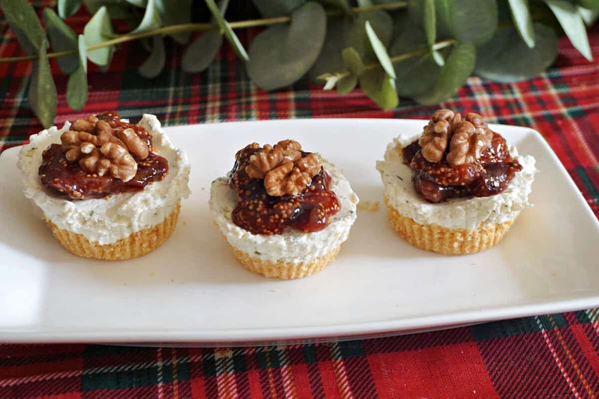 A white rectangle plate with 3 cheesecakes topped with fig jam and walnut halves.