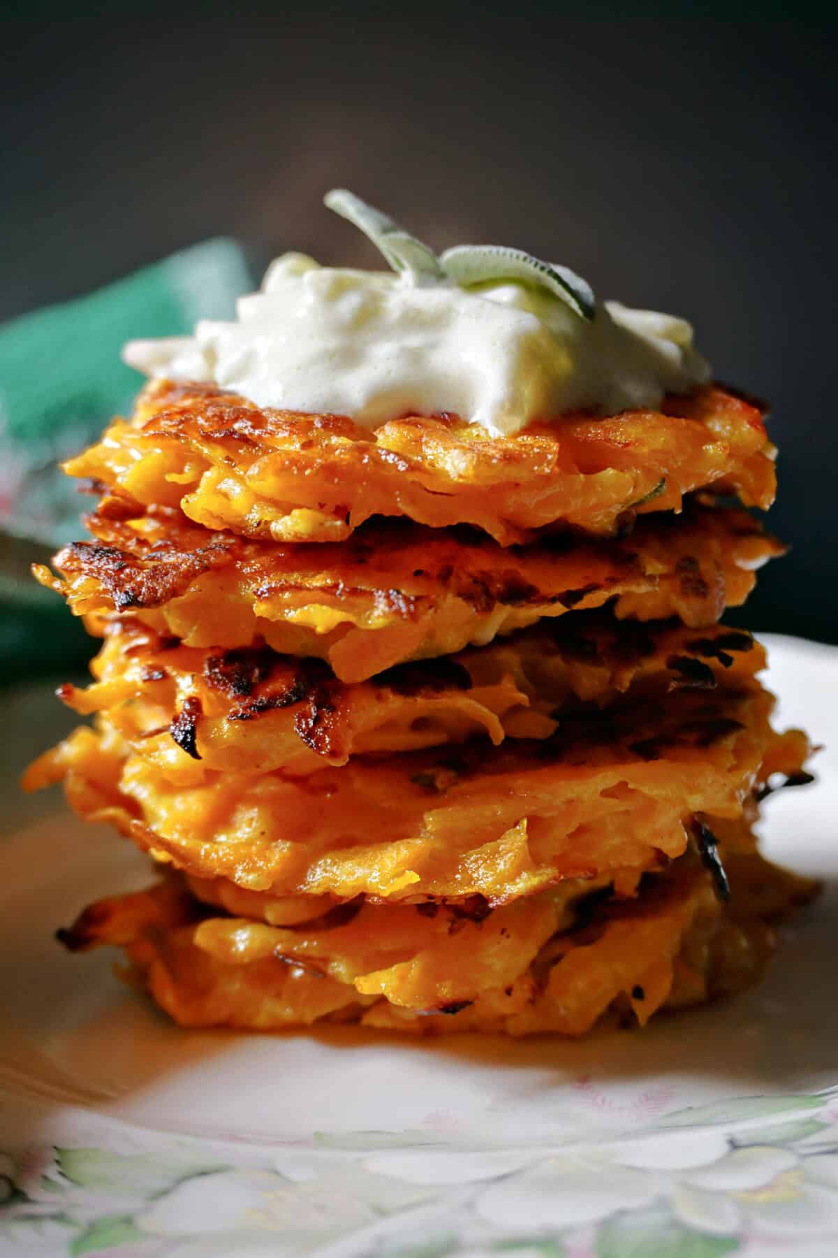 A pile of butternut squash fritters topped with tzatziki and sage leaves.
