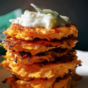 A stack of butternut squash fritters topped with tzatziki and sage leaves.