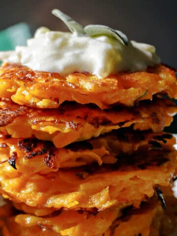 A stack of butternut squash fritters topped with tzatziki and sage leaves.