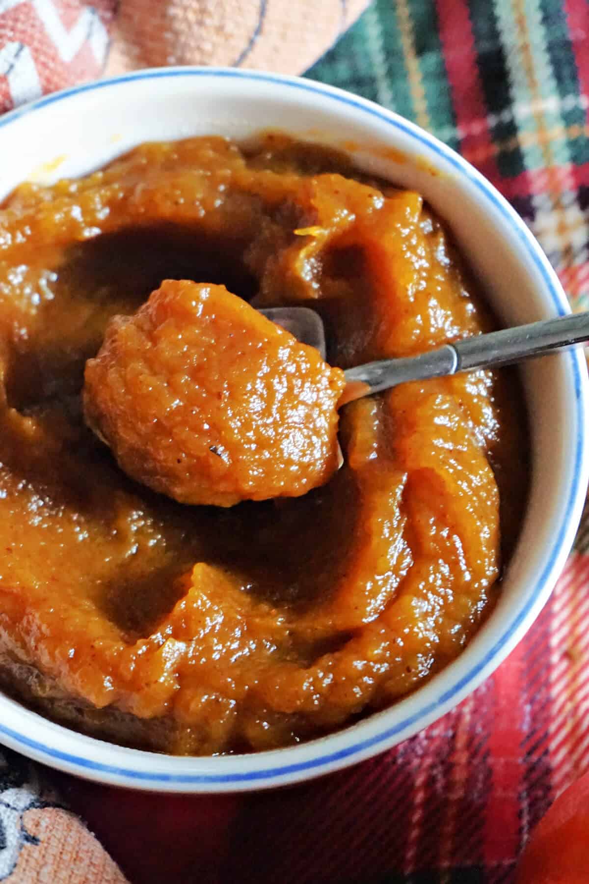 A white ramekin with pumpkin butter and a teaspoon sitting in it.