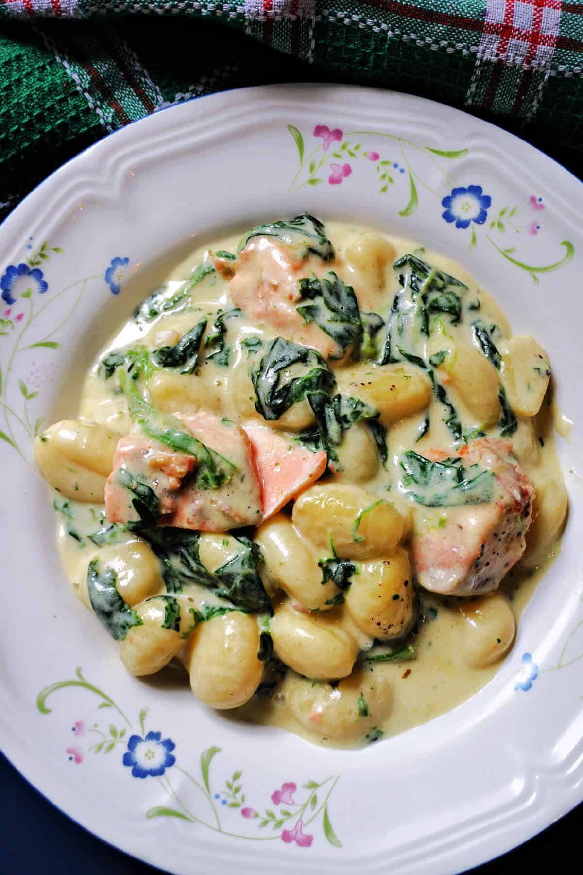 A white plate with a portion of creamy gnocchi with spinach and salmon pieces.