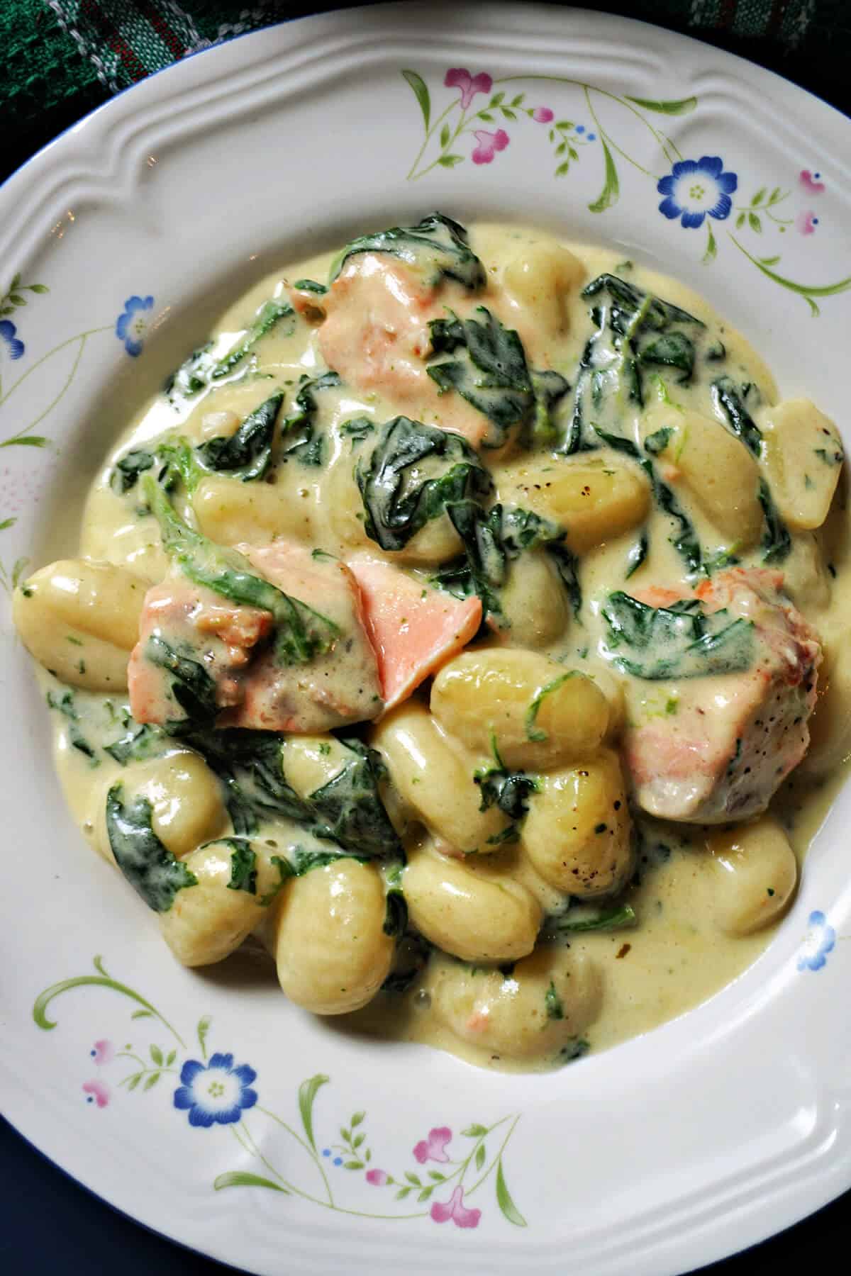 A white plate with a portion of gnocchi with salmon chunks and spinach.