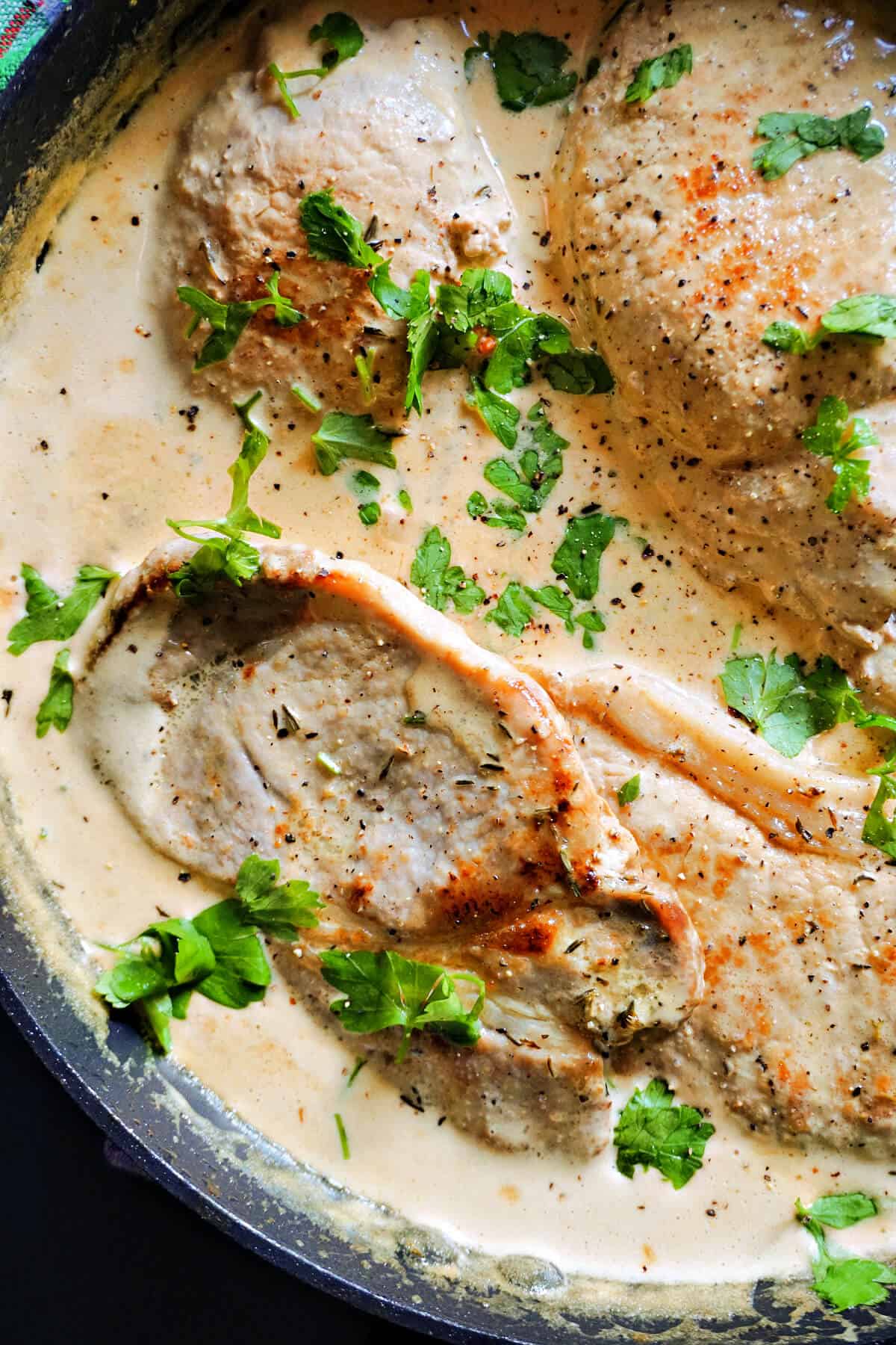 Close-up of a pan with pork steak in a creamy sauce, garnished with chopped parsley.