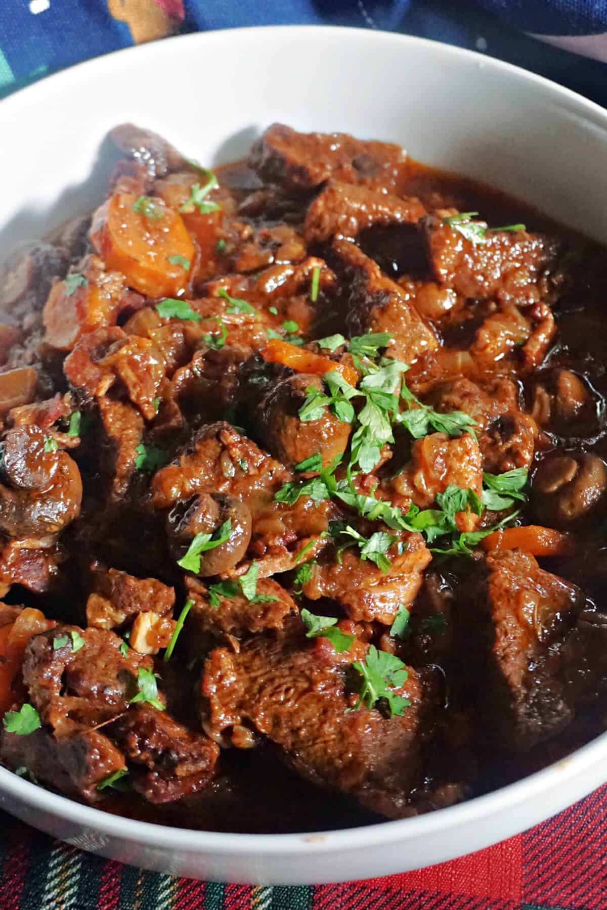 A white bowl with a portion of beef stew garnished with chopped parsley.
