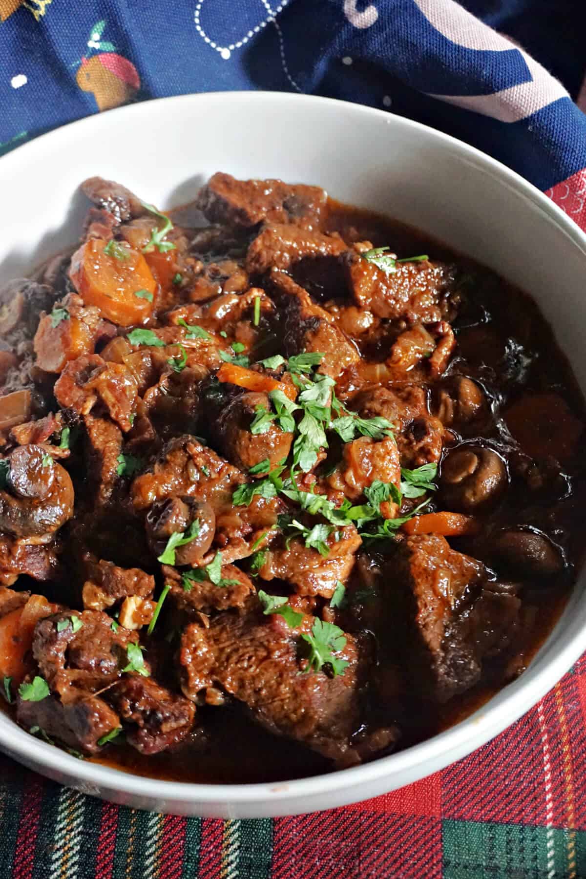 A white bowl with a portion of beef stew garnished with chopped parsley.